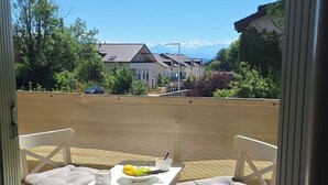 Een balkon met twee witte stoelen en een tafeltje, een schaal fruit en een beker.