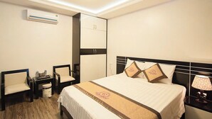 A hotel room with a bed, two chairs, a nightstand, a lamp, an air conditioning unit, and a wardrobe. - Halong Mackeno Hotel (Bai Chay)