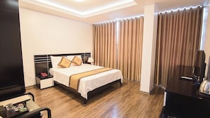 A hotel room with a bed, bedside table, lamp, curtains, and a desk with a computer. - Halong Mackeno Hotel (Bai Chay)