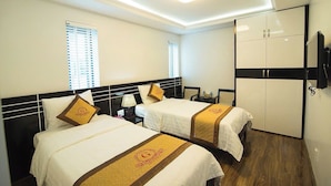 A hotel room with two beds, a wardrobe, and a desk with a lamp. - Halong Mackeno Hotel (Bai Chay)