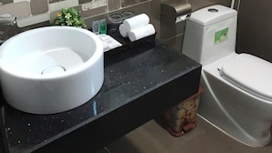 A bathroom with a black countertop, a white sink, a toilet, and a tiled backsplash. - Halong Mackeno Hotel (Bai Chay)