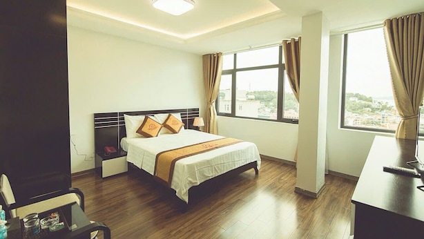 A hotel room with a bed, bedside table, lamp, and a desk with a computer. - Halong Mackeno Hotel (Bai Chay)