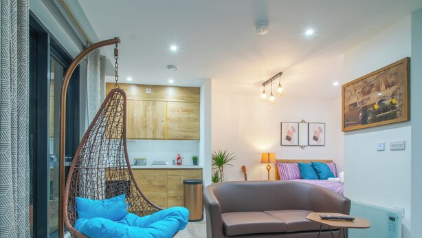 Un salon moderne avec un fauteuil suspendu, un canapé, une petite table et un coin cuisine à l’arrière-plan.
