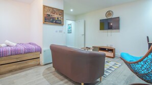 Un salon moderne avec un canapé, un fauteuil, un téléviseur et un lit recouvert d’une couverture à rayures.