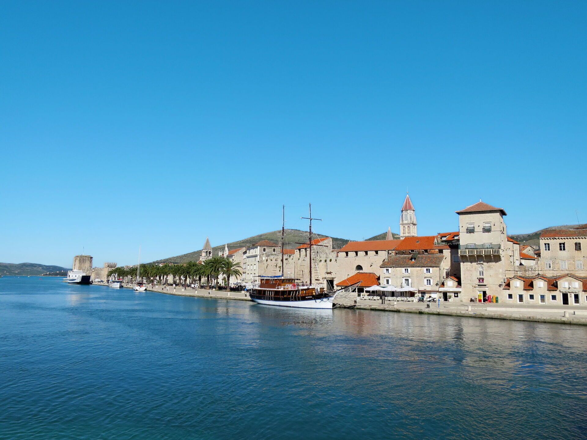 A coastal town with historic buildings, a prominent tower, and a calm harbor with boats.