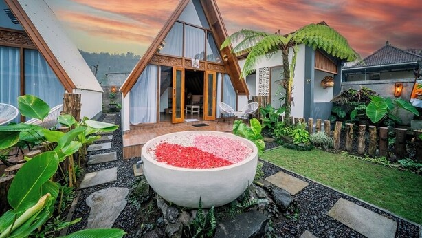 A modern house with a triangular roof, a large garden with a decorative stone basin, and a view of the sky.