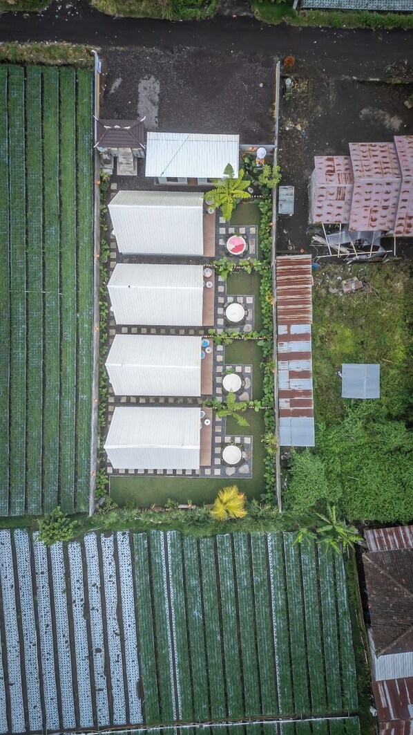 Vista aérea de una propiedad con varios edificios grandes de techos blancos, un patio central con mobiliario y zonas verdes circundantes.