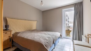 A bedroom with a bed, a nightstand, a lamp, a chair, and a view of the outside. - Seastar 0202 met garage (NIEUWPOORT)