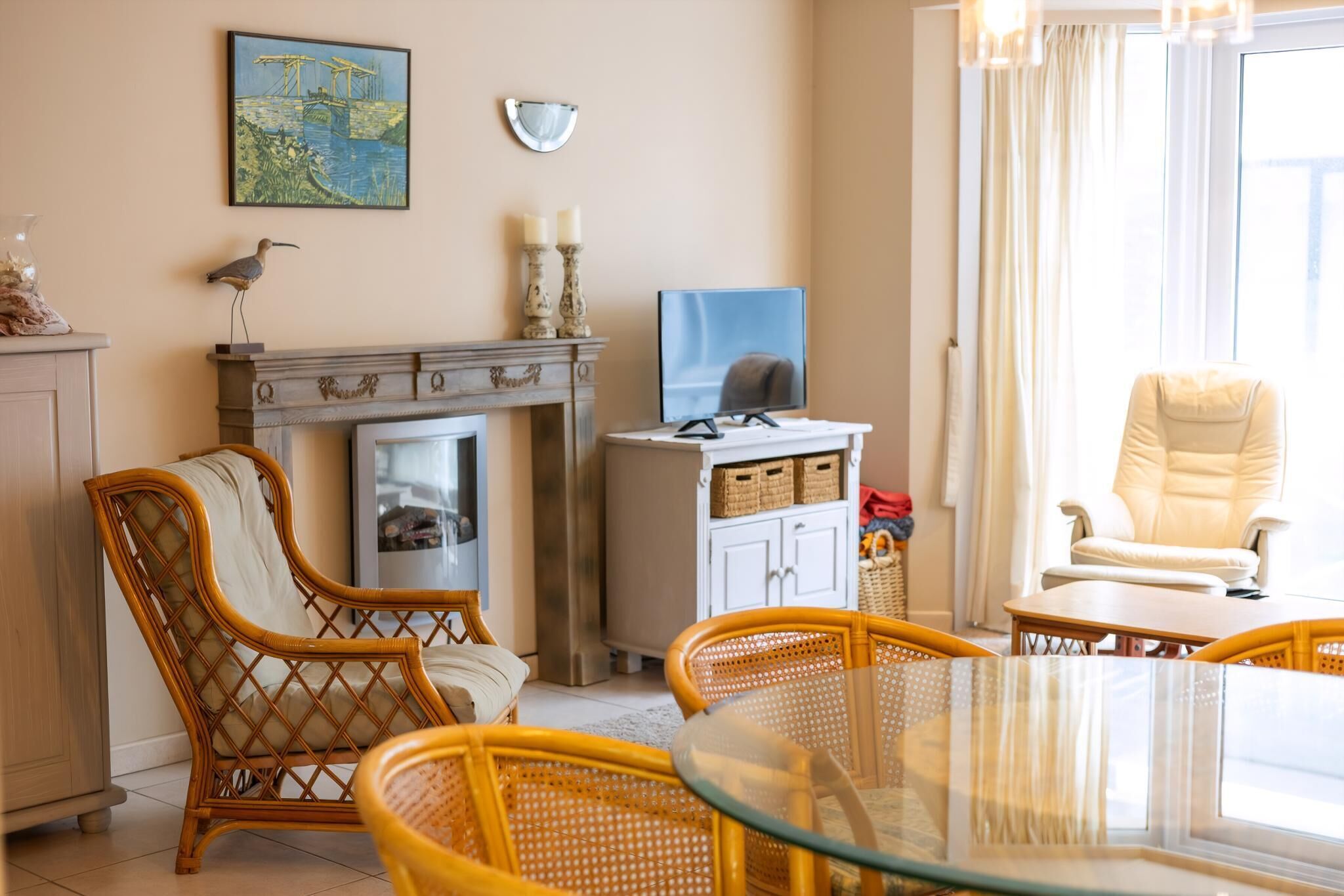 Una sala de estar con sillones de mimbre, una mesa de vidrio, chimenea, televisor y un ventanal grande.