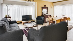 A living room with a sofa, TV, dining table, chairs, and a large mirror.