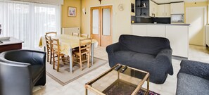 Ein Wohnzimmer mit einer Couch, einem Couchtisch, einem Esstisch mit Stühlen und einer Küchenzeile mit Schränken und Geräten.