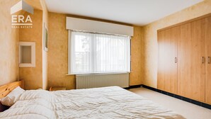 A bedroom with a bed, a window with blinds, a radiator, and a wardrobe.