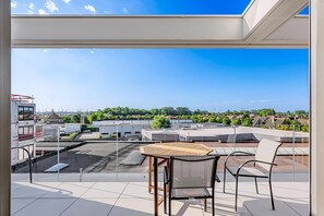 A balcony with a table and chairs, offering a view of a parking lot and buildings.
