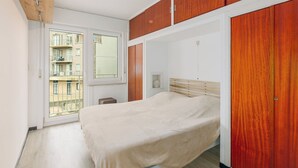 Un dormitorio con cama, armario de madera y ventana con vistas a edificios.