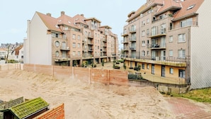 Un edificio residencial de varios pisos con balcones, un patio interior y una zona arenosa al frente.