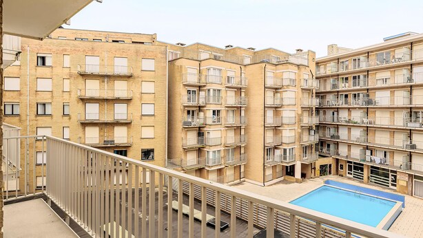 Een meerlaags appartementencomplex met balkons, een zwembad en een poort.