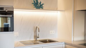 Een moderne keuken met een roestvrijstalen spoelbak, witte kasten en een marmeren achterwand.