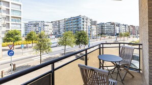 En balkong med ett bord och stolar, med utsikt över en gata med hus och träd.