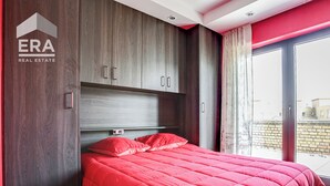 A bedroom with a large bed, wooden wardrobe, and a sliding glass door to a balcony. - Gouden Boom 0618 + P* (Koksijde)