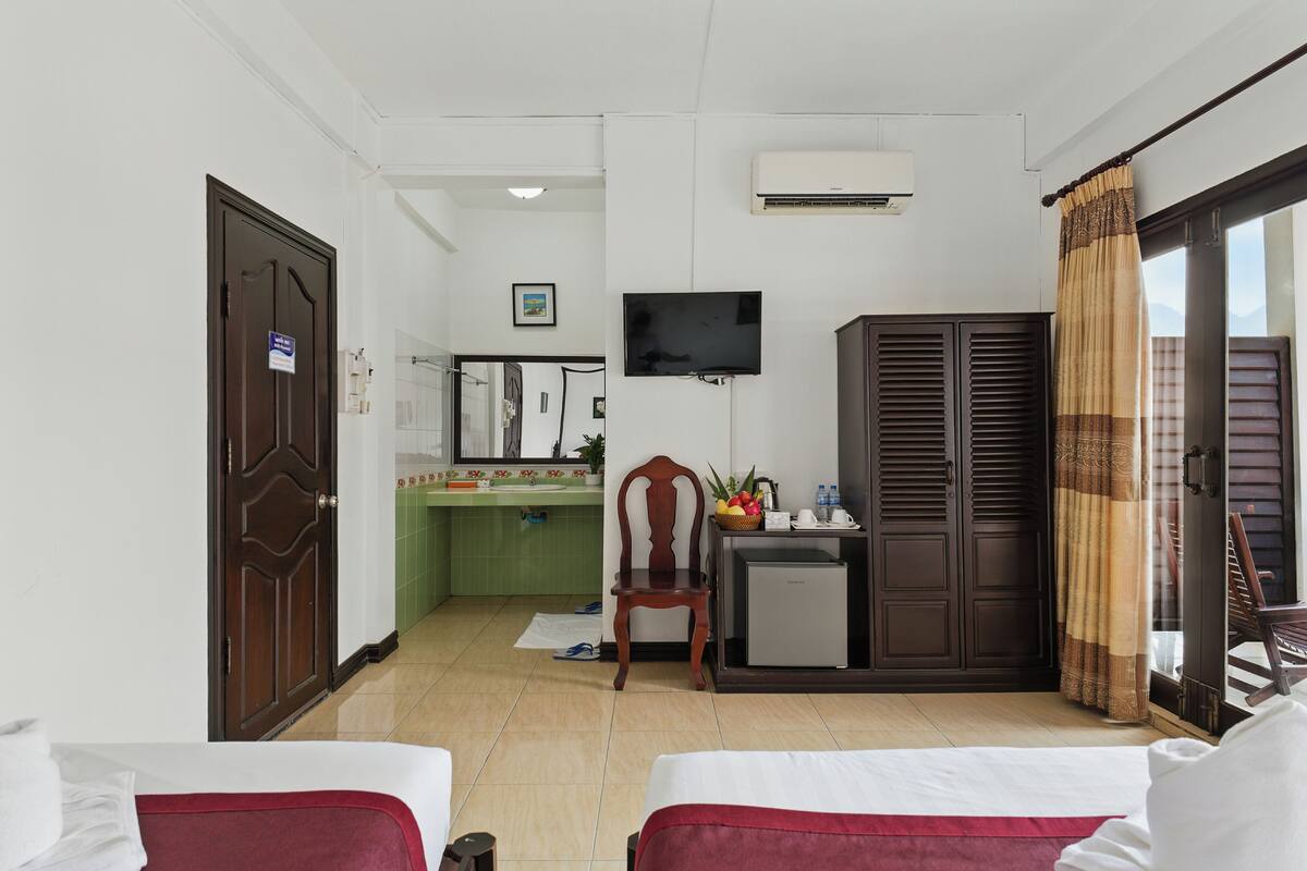 Una habitación de hotel con dos camas, un escritorio con computadora, un televisor y un armario.