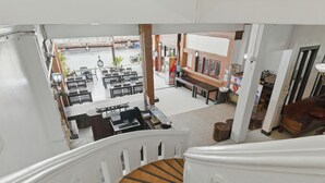 A view from a second-floor balcony overlooking a dining area with tables and chairs, a staircase with wooden steps, and a brick wall. - Central Hotel Vang Vieng (Vang Vieng)