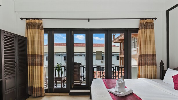 A hotel room with a bed, a red throw, a tray with a towel, and a view of the outside balcony. - Central Hotel Vang Vieng (Vang Vieng)