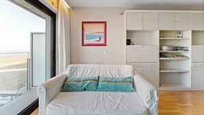 A modern living room with a white sofa, teal cushions, a framed picture on the wall, and a white cabinet with shelves. - 1 bedroom accommodation in De Panne (De Panne)