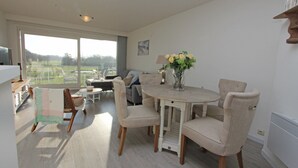 A spacious living room with a dining area, large windows, and a view of a green landscape.