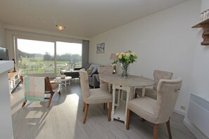 A spacious living room with a dining area, large windows, and a view of a green landscape.