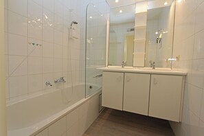 Ein modernes Badezimmer mit einer Duschkabine aus Glas, einer weißen Badewanne und einem Waschtisch mit Spiegel.