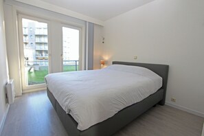 Ein Schlafzimmer mit einem Bett, einer Schiebetür zum Balkon und einem Nachttisch mit einer Lampe.