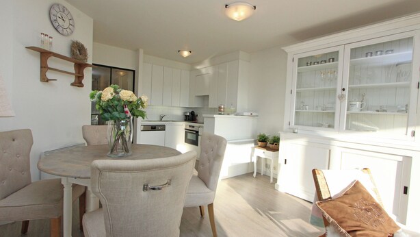 A modern kitchen with white cabinets, a dining area with a round table and chairs, and a built-in cabinet with glassware.
