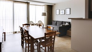 A modern living room with a dining table and chairs, a grey sofa, and a large window with curtains. - 3 bedroom accommodation in Koksijde (Koksijde)