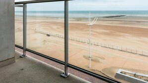 A view of a beach from inside a building with large windows, featuring a sandy beach, a metal fence, and a lamppost. - 3 bedroom accommodation in Koksijde (Koksijde)