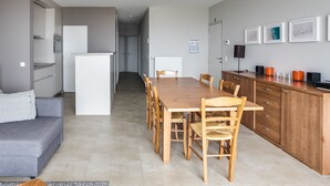 A modern kitchen with a dining table and chairs, a grey sofa, and a wooden cabinet with orange containers. - 3 bedroom accommodation in Koksijde (Koksijde)