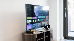 Una TV a schermo piatto su un supporto in legno, con un telecomando e un oggetto decorativo accanto.