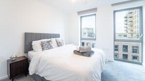 Una camera da letto moderna con un letto grande, un comodino, una finestra con vista sulla città e una lampada a sospensione.