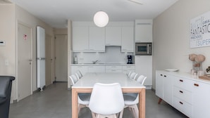 Une cuisine moderne avec des meubles blancs, une grande table à manger avec des chaises, un four à micro-ondes et une machine à café.