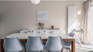 Un espace repas moderne avec une table blanche et des chaises grises, un élément décoratif mural et une lampe près de la fenêtre.