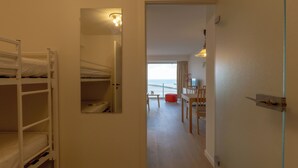 A room with bunk beds, a small table, and a chair. There is a door leading to another room with a view. - 1 bedroom accommodation in Nieuwpoort (Nieuwpoort)