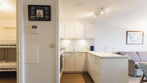A compact kitchen with white cabinets, a built-in oven, and a sink. There is a small island with a coffee machine, and a framed picture on the wall. - 1 bedroom accommodation in Nieuwpoort (Nieuwpoort)
