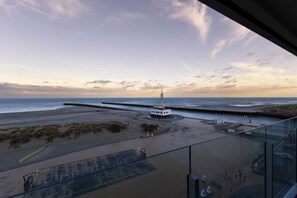 A beach view from a balcony with a pier extending into the water, a small building near the shore, and a basketball court.