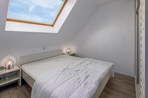 Une chambre à coucher avec un puits de lumière, un lit, des tables de chevet et une commode.