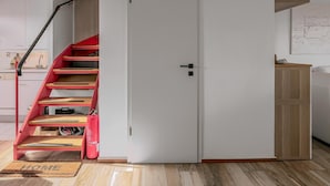 A modern kitchen with white cabinets, a wooden countertop, and a red spiral staircase leading to a white door. - 2 bedroom accommodation in Koksijde (Koksijde)