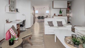 A modern living room with a white sofa, a dining area with a table and chairs, and a kitchen area with cabinets and a countertop. - 2 bedroom accommodation in Koksijde (Koksijde)