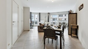 Zona pranzo moderna con tavolo e sedie, un divano e vista sugli edifici attraverso ampie finestre.