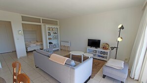 Un salon moderne avec un canapé gris, une petite table ronde, un téléviseur et une bibliothèque.