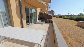 Un balcon avec une table et des chaises blanches, un pot de fleurs et une vue sur un espace verdoyant et des bâtiments en arrière-plan.