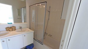 Une salle de bain avec deux lavabos, une douche et un miroir.