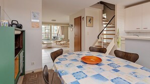 A dining area with a table set for four, a staircase, and a kitchen area with cabinets. - ZeeZonZand C-0206 + G* (Koksijde)